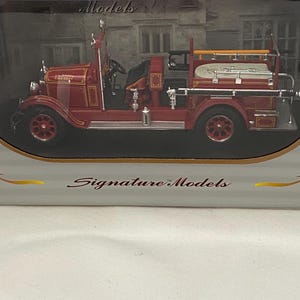 May include: A red vintage fire truck model with gold accents. The model has a ladder, hose, and other details. The words "Models" and "Signature Models" are visible on the packaging.