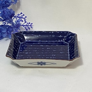May include: Rectangular ceramic dish with a blue and white design. The dish has a dark blue interior with a subtle pattern and a white exterior with a floral design. The rim is a dark brown color. Decorative tableware.
