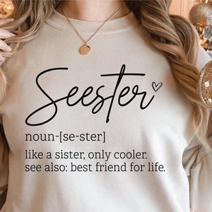 以下が含まれることがあります： クリーム色のスウェットシャツに、ハートマーク付きの筆記体で「Seester」という言葉が書かれています。下のテキストでは、この言葉は「姉妹のようなものだが、もっとクール」と定義されています。また、「参照：生涯の親友」とも書かれています。