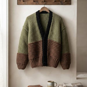 May include: A chunky knit cardigan featuring a colour-blocked design with olive green upper sections and brown lower sections. The garment has a black V-neckline with a cable knit trim, long sleeves with brown cuffs, and a button-down front closure.