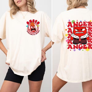May include: A white t-shirt with a red cartoon character on the front and the text "Anger It's OK to Feel All the Feels". The back of the shirt has the word "Anger" repeated in a circle with colorful dots.