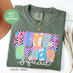 a green t-shirt with a colorful design that says "First Grade Squad" printed on it.