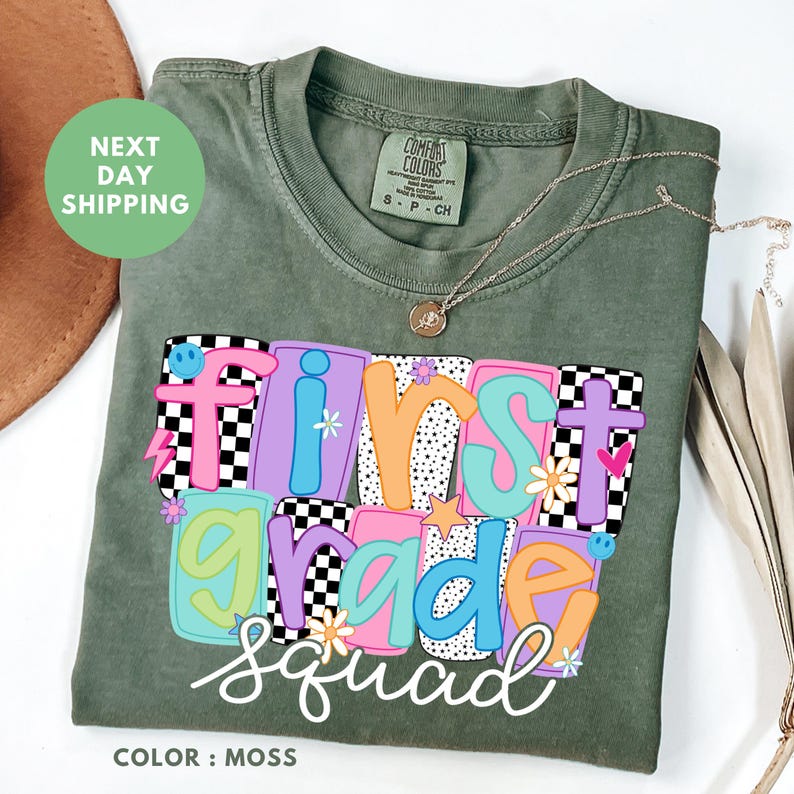 a green t-shirt with a colorful design that says "First Grade Squad" printed on it.