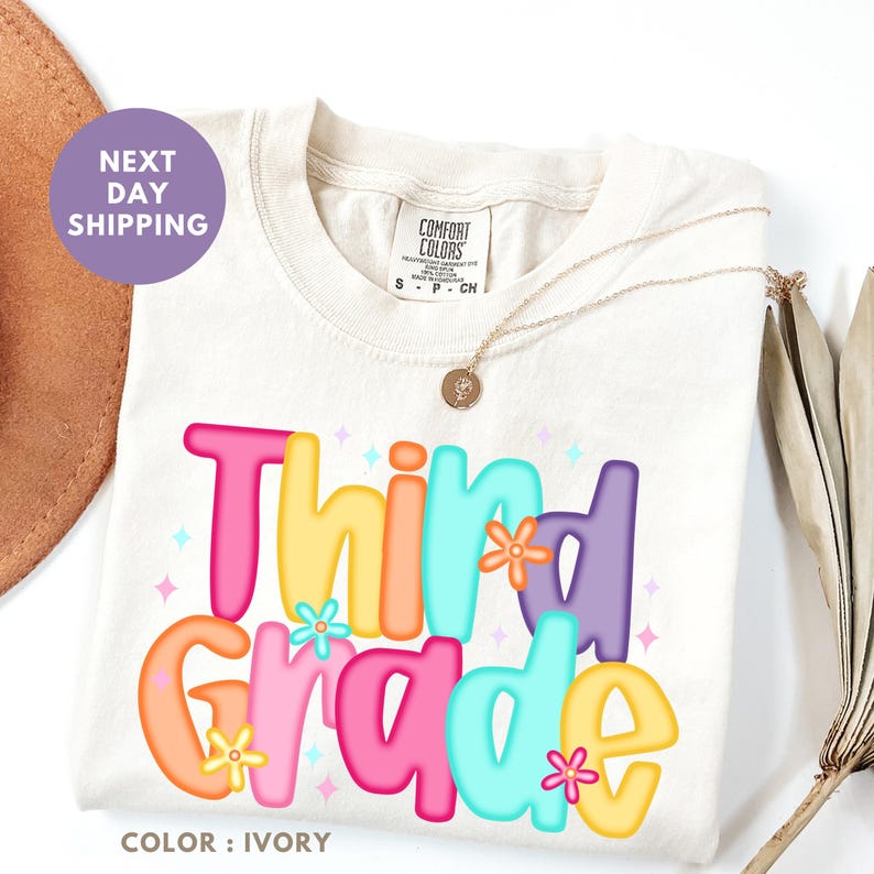 a white t-shirt with a colorful graphic design that says "Third Grade" in a playful font.