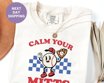 May include: Ivory t-shirt featuring a baseball graphic and the text "Calm Your Mitts".