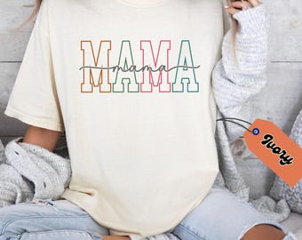 May include: A white t-shirt with the word "MAMA" in colorful outlined letters. The word "mama" is written in cursive underneath the letters.
