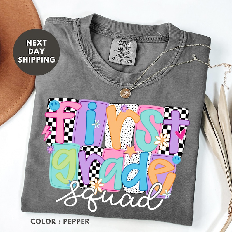 a gray t-shirt with a colorful design that says "First Grade Squad" in a playful font.