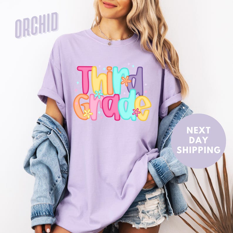A woman wearing a purple t-shirt with the text "Third Grade" printed on it, standing in front of a white background.