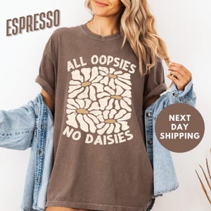 May include: A brown t-shirt with a white daisy graphic and the text "All oopsies no daisies".