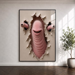 Peut inclure: Impression artistique encadrée représentant une créature rose et poilue perçant une surface en papier déchiré. La créature a une bouche souriante et deux grands yeux. L'œuvre est encadrée en noir et se détache sur un fond neutre.