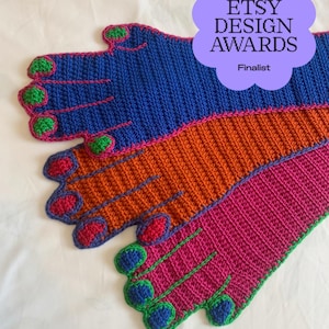 May include: Three crocheted hand-shaped gloves in blue, orange, and magenta. The blue glove has green fingertips, the orange glove has red fingertips, and the magenta glove has blue fingertips. A purple badge reads 2026 ETSY DESIGN AWARDS Finalist.