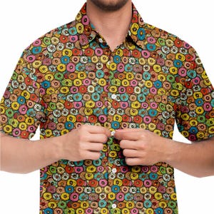 Puede incluir: Una camisa de manga corta con botones y un estampado de donuts coloridos. La camisa está hecha de una tela ligera y tiene un corte holgado.