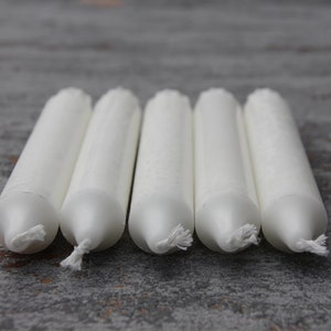 May include: Five white taper candles arranged in a row on a gray textured surface.