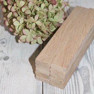 May include: A stack of wooden planks, likely oak, with a natural wood finish. The planks are arranged in a neat pile, with the grain of the wood visible. The planks are a light brown color.