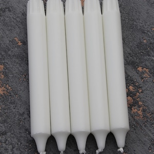 May include: Five white taper candles with a textured top and a pointed bottom. The candles are arranged in a row on a gray textured surface.