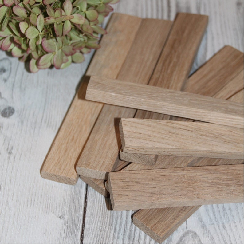 May include: A pile of unfinished, light brown wooden strips. The strips are stacked on top of each other and are all the same size. The strips are smooth and have a natural wood finish.