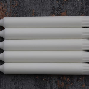 May include: Five white taper candles with a fluted design at the top. The candles are arranged in a stack.