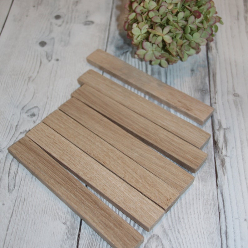 May include: A set of seven natural wood strips, arranged in a fan shape on a white wood surface. The strips are all the same width and length, and they are smooth and polished.