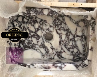 Puede incluir: Un lavabo de mármol blanco con vetas moradas y grises. El lavabo es rectangular con bordes redondeados y tiene un solo agujero de drenaje. El lavabo está hecho a mano y es 100% original.