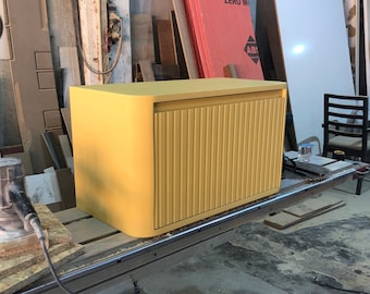 May include: A yellow cabinet with a ribbed door. The cabinet is sitting on a workbench in a workshop.