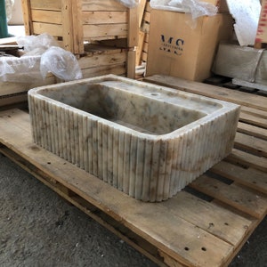 Puede incluir: Un lavabo de mármol blanco de forma rectangular con un borde acanalado. El lavabo está sobre una tarima de madera.