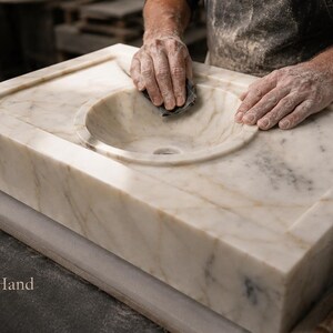 Handmade marble sink being shaped by a stone master in the workshop, with round basin detail, thick marble block and visible handcrafted finishing process