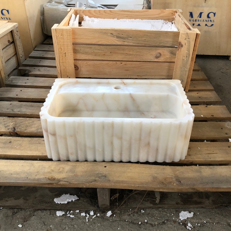 May include: A white marble sink with a fluted design. The sink is sitting on a wooden pallet.