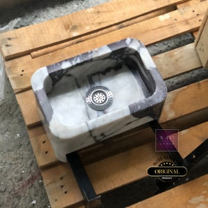 Overhead angled view of the marble powder room sink showing the fitted drain, compact shape and natural purple stone veins.