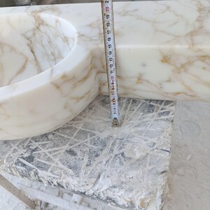 Luxurious wall-mounted Calacatta marble sink carved from a single block. Featuring 3 faucet holes, fluted front design, and floating vanity look. Ideal for modern, minimalist bathrooms. Custom sizes available. Handmade from natural Italian stone. Bathroom sink, marble vanity, stone basin, designer sink, fluted marble, wall mount sink, handmade sink, rectangular sink, luxury bathroom decor.