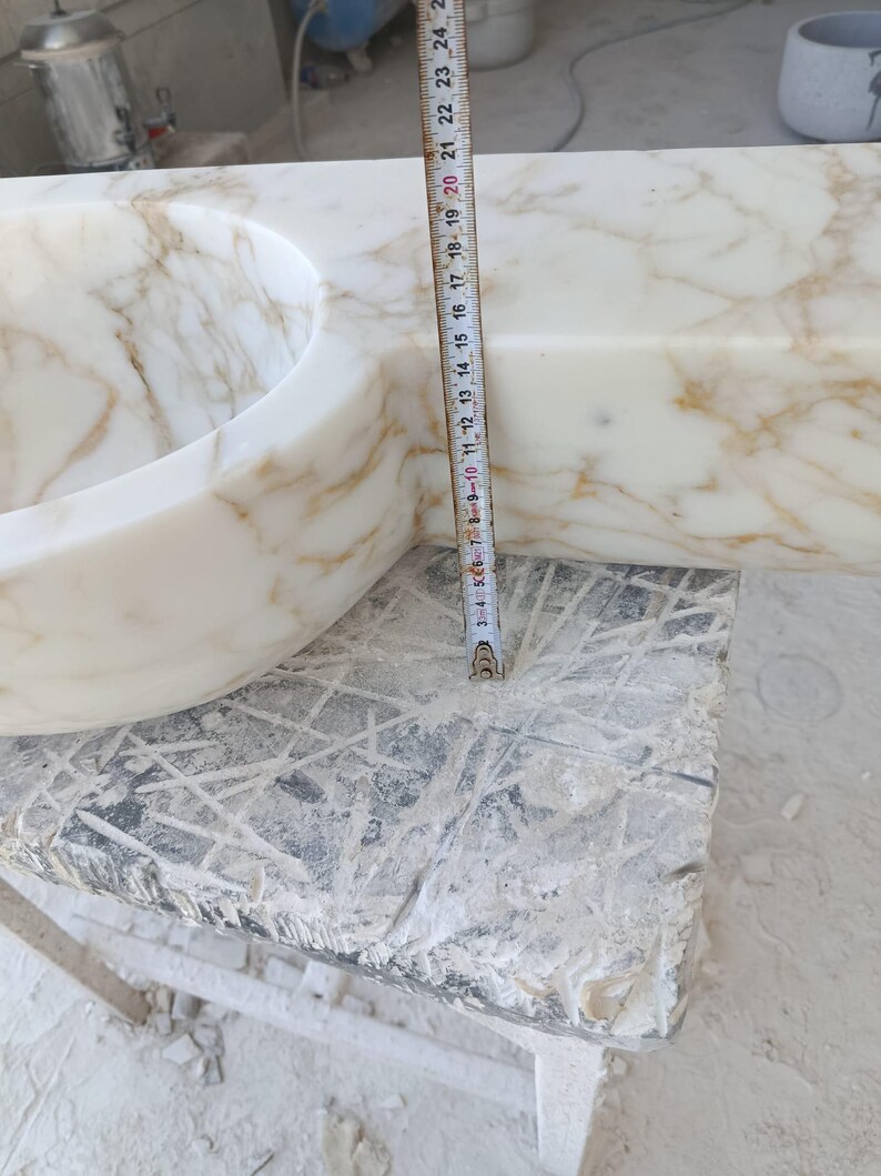 Luxurious wall-mounted Calacatta marble sink carved from a single block. Featuring 3 faucet holes, fluted front design, and floating vanity look. Ideal for modern, minimalist bathrooms. Custom sizes available. Handmade from natural Italian stone. Bathroom sink, marble vanity, stone basin, designer sink, fluted marble, wall mount sink, handmade sink, rectangular sink, luxury bathroom decor.