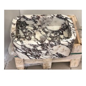 May include: A white marble sink with purple and brown veining. The sink is rectangular with rounded edges and has a single drain hole.