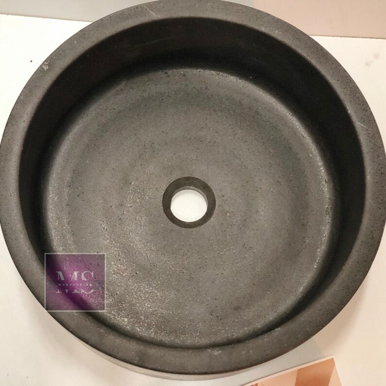 Pu&ograve; includere: Un lavandino rotondo in cemento nero con un foro di scarico al centro. Il lavandino &egrave; progettato per un bagno o una cucina.