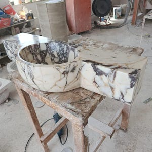 Luxurious wall-mounted Calacatta marble sink carved from a single block. Featuring 3 faucet holes, fluted front design, and floating vanity look. Ideal for modern, minimalist bathrooms. Custom sizes available. Handmade from natural Italian stone. Bathroom sink, marble vanity, stone basin, designer sink, fluted marble, wall mount sink, handmade sink, rectangular sink, luxury bathroom decor.