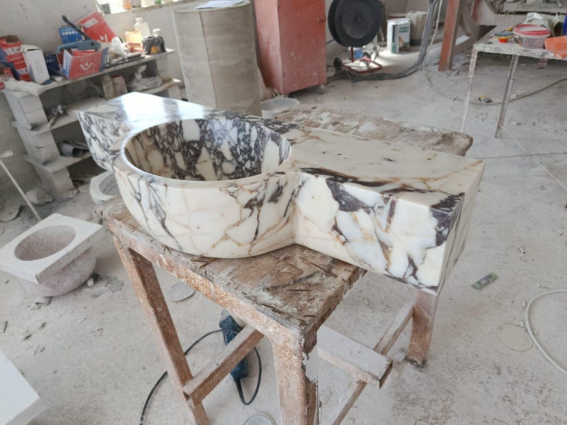 Luxurious wall-mounted Calacatta marble sink carved from a single block. Featuring 3 faucet holes, fluted front design, and floating vanity look. Ideal for modern, minimalist bathrooms. Custom sizes available. Handmade from natural Italian stone. Bathroom sink, marble vanity, stone basin, designer sink, fluted marble, wall mount sink, handmade sink, rectangular sink, luxury bathroom decor.