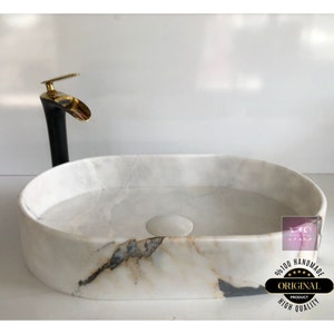 May include: White oval marble sink with a black and gold faucet. The sink has a unique marbled pattern and is handmade. The text on the sink reads "100% Handmade Original Product High Quality".