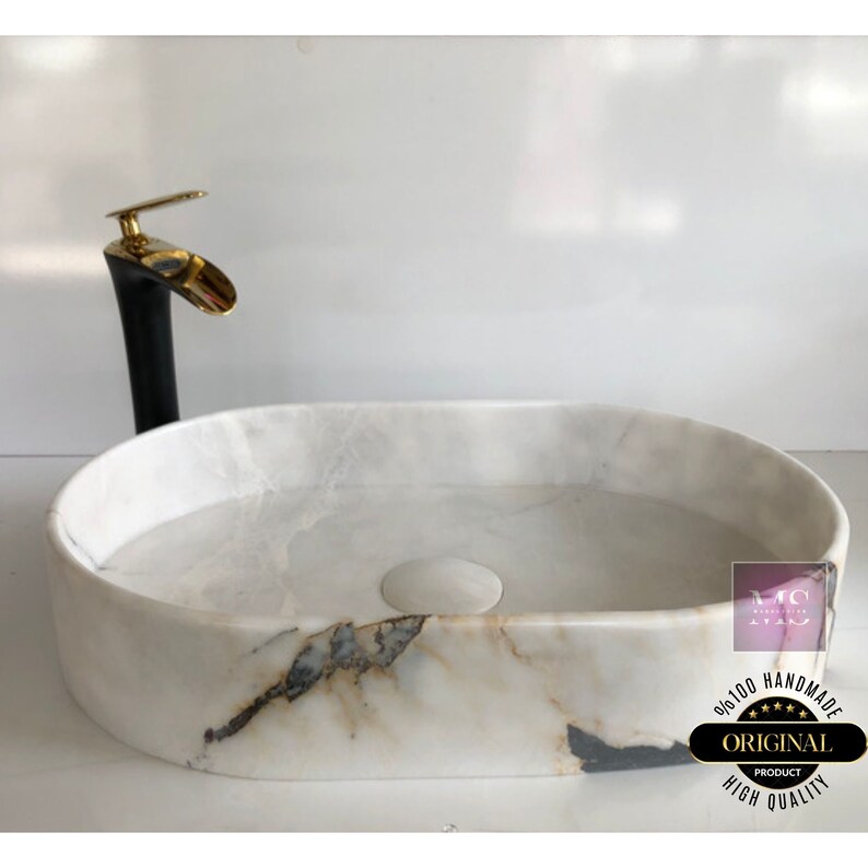 May include: White oval marble sink with a black and gold faucet. The sink has a unique marbled pattern and is handmade. The text on the sink reads "100% Handmade Original Product High Quality".