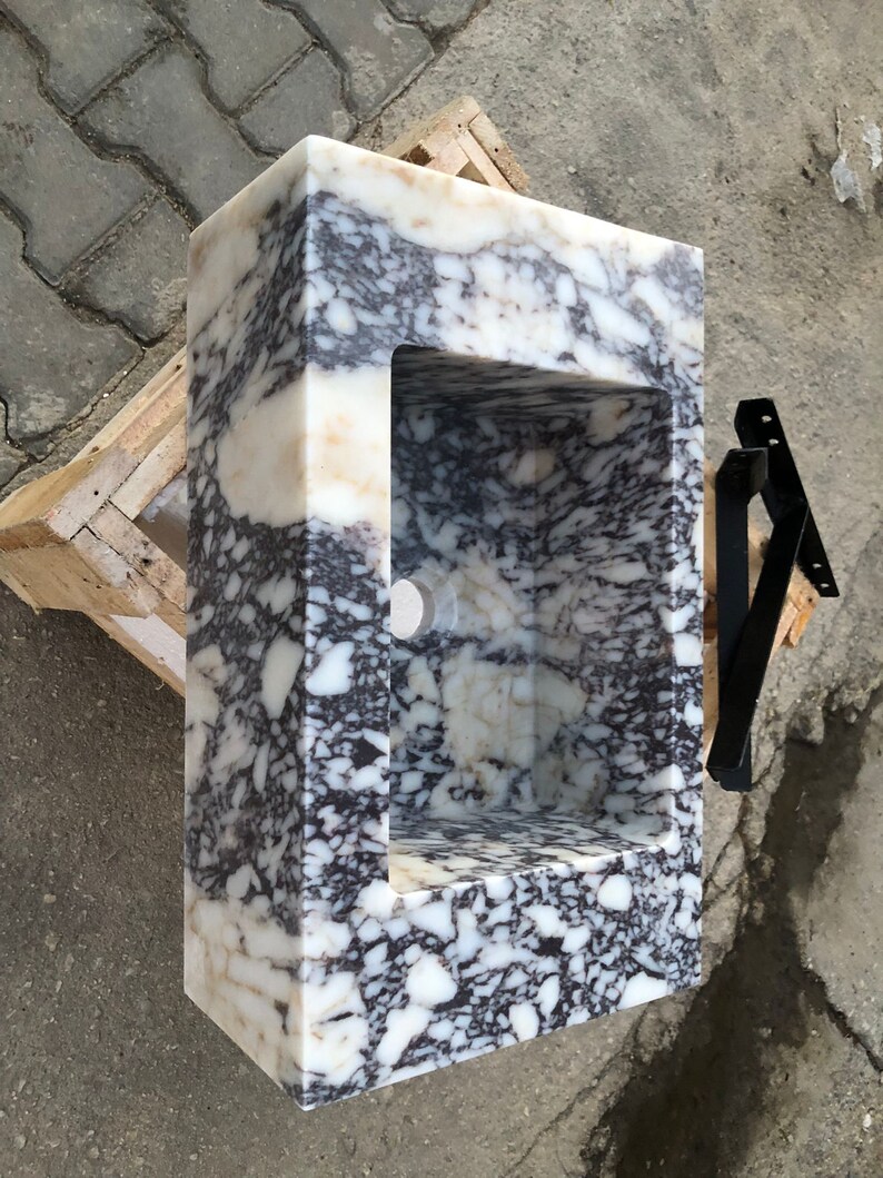 May include: A white marble sink with a black and white veined pattern. The sink is rectangular and has a square cutout for the basin. The sink is sitting on a wooden platform.