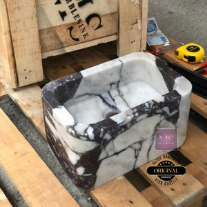 Front three-quarter view of the purple and white marble sink with an open drain hole and distinctive Calacatta Viola pattern.