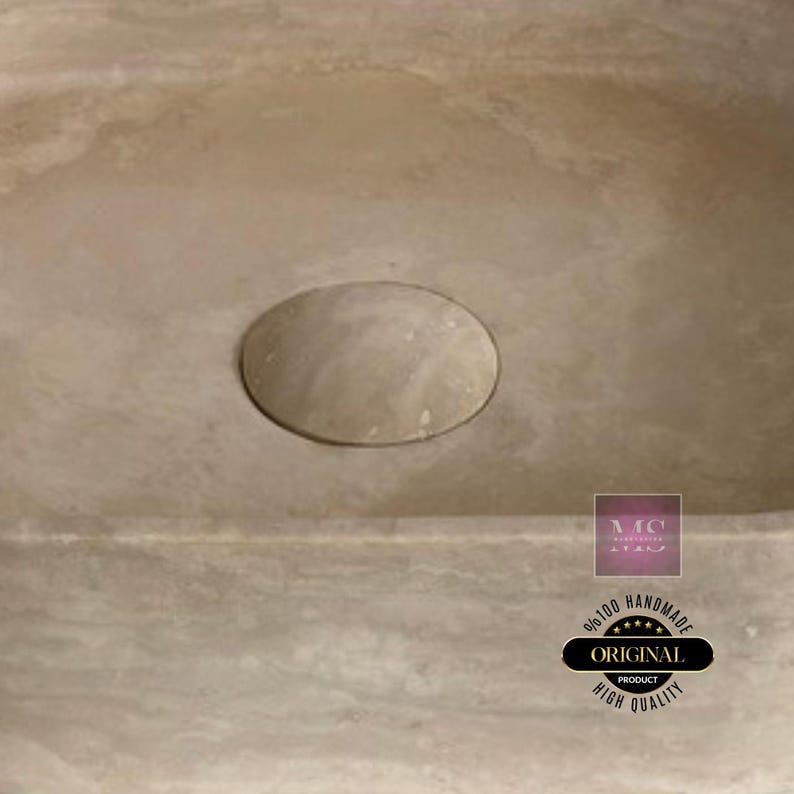 Puede incluir: Primer plano de un lavabo de piedra de color marr&oacute;n claro con un desag&uuml;e circular. El lavabo est&aacute; hecho de piedra natural y tiene un acabado liso y pulido. El desag&uuml;e est&aacute; centrado en el lavabo y est&aacute; rodeado por un borde ligeramente elevado.