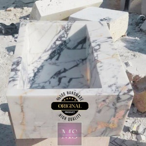 May include: A white marble sink with a rectangular shape and a unique design. The sink is handmade and features a label that says "100% Handmade Original Product High Quality".