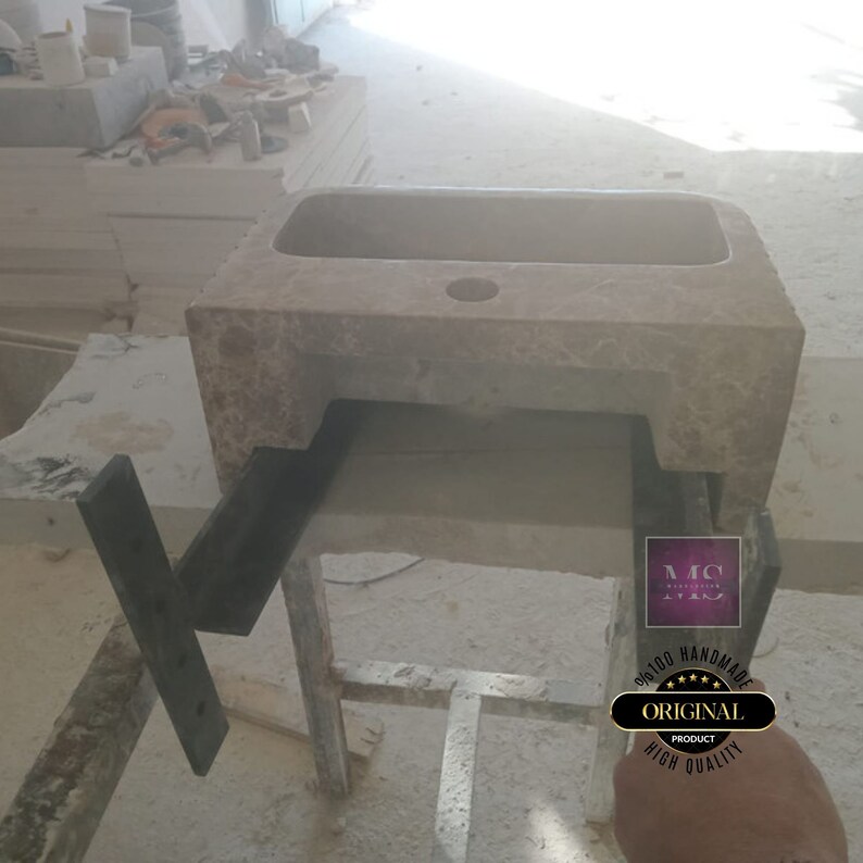 May include: A stone sink with a single drain hole, sitting on a metal frame. The sink is beige with brown marbling. The frame is black metal. The sink is handmade and is a high quality product.