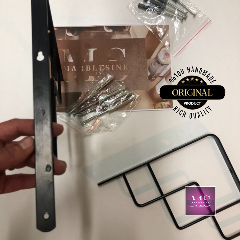 Puede incluir: Dos soportes de estanter&iacute;a de metal negro con tornillos. Los soportes est&aacute;n dise&ntilde;ados para montarse en una pared. La imagen tambi&eacute;n incluye una peque&ntilde;a bolsa de tornillos y una tarjeta con el texto "MARBLESINK 100% HANDMADE ORIGINAL PRODUCT HIGH QUALITY".