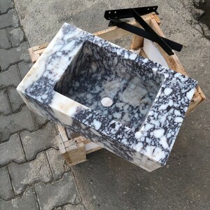 May include: A white and black marble sink with a rectangular shape. The sink is sitting on a wooden pallet.