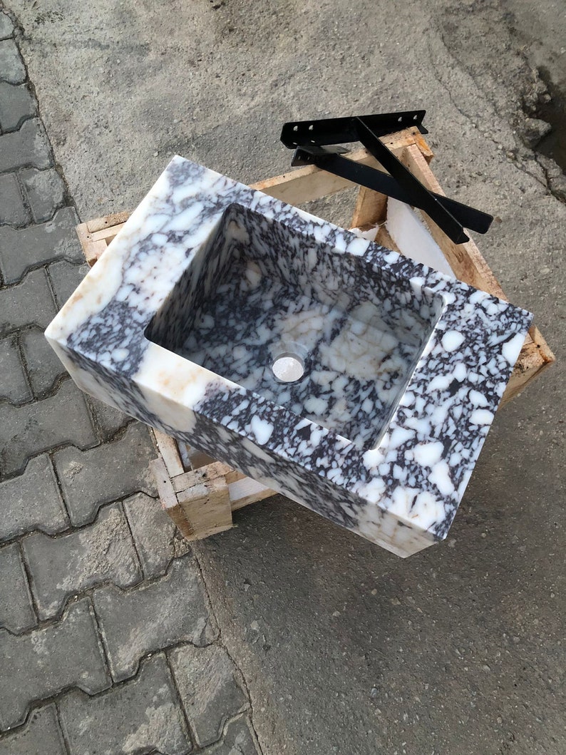 May include: A white and black marble sink with a rectangular shape. The sink is sitting on a wooden pallet.