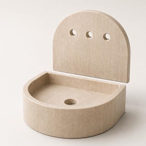 May include: A beige stone wall-mounted sink featuring a semi-circular basin and a tall, arched back panel. The back panel includes three circular holes arranged horizontally, while the basin base contains a single central drainage hole.