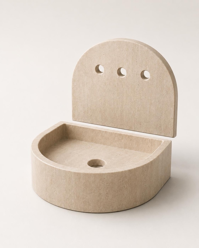 May include: A beige stone wall-mounted sink featuring a semi-circular basin and a tall, arched back panel. The back panel includes three circular holes arranged horizontally, while the basin base contains a single central drainage hole.