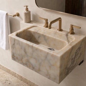 Wall-mounted Calacatta Viola marble sink installed in a modern powder room with brushed brass three-hole faucet, rounded mirror and white towel, showing the deep rectangular basin and natural cream veining.
