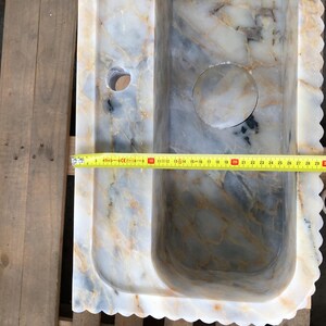 May include: A white marble sink with a wavy edge and a drain hole. The sink is 76 cm long.