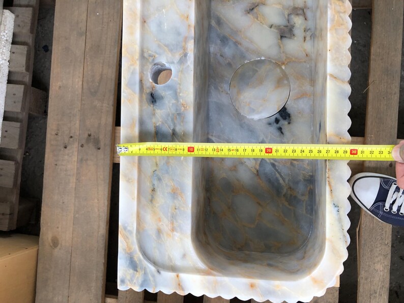 May include: A white marble sink with a wavy edge and a drain hole. The sink is 76 cm long.