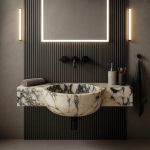 Luxurious wall-mounted Calacatta marble sink carved from a single block. Featuring 3 faucet holes, fluted front design, and floating vanity look. Ideal for modern, minimalist bathrooms. Custom sizes available. Handmade from natural Italian stone. Bathroom sink, marble vanity, stone basin, designer sink, fluted marble, wall mount sink, handmade sink, rectangular sink, luxury bathroom decor.